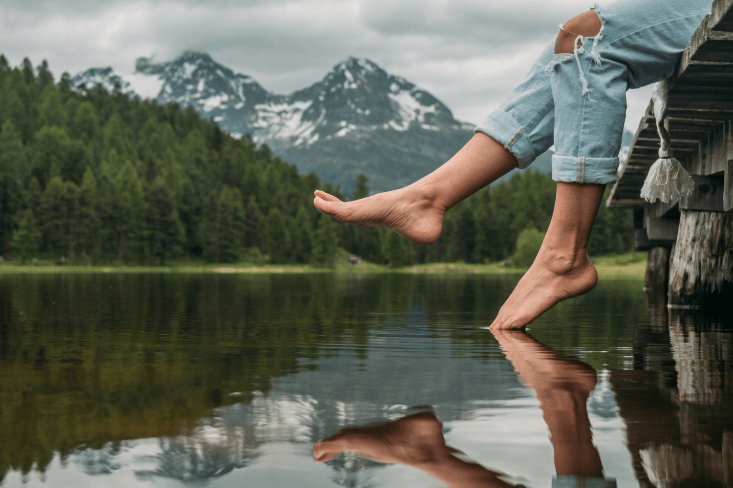 Feet dangling off jetty by a lake in the mountains